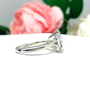 Elegant 4-prong sterling silver cathedral engagement ring set featuring a 12x8mm precision-cut pear cubic zirconia.  Displayed on a white surface with soft pastel floral background.