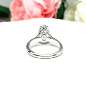 Elegant 4-prong sterling silver cathedral engagement ring set featuring a 12x8mm precision-cut pear cubic zirconia.  Displayed on a white surface with soft pastel floral background.