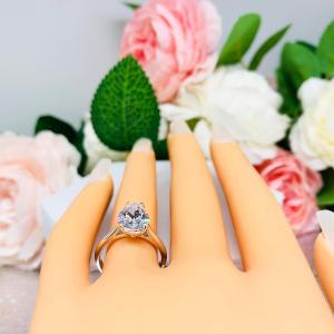 Mannequin hand with long white shimmery nails, displayed against a soft white-gray background with pink and white floral accents. The hand is wearing an elegant 4-prong sterling silver cathedral engagement ring featuring a 12x8mm precision-cut pear cubic zirconia.