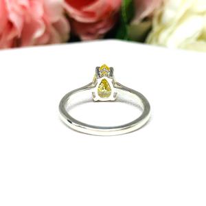 A sterling silver engagement ring set with a 9x6mm pear-cut canary yellow cz. Displayed on a white surface with soft pastel floral background.