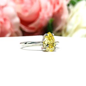 A sterling silver engagement ring set with a 9x6mm pear-cut canary yellow cz. Displayed on a white surface with soft pastel floral background.