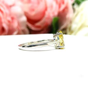 A sterling silver engagement ring set with a 9x6mm pear-cut canary yellow cz. Displayed on a white surface with soft pastel floral background.
