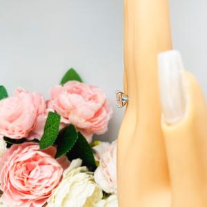 Mannequin hand with long white shimmery nails, displayed against a soft white-gray background with pink and white floral accents. The hand is wearing a sterling silver solitaire cathedral engagement ring set with a 10x8mm emerald cut cubic zirconia.