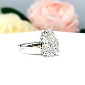 An elegant 4-prong sterling silver engagement ring with a 3mm wide band featuring a 13x9mm near colorless precision-cut pear cubic zirconia. Displayed on a white surface with a floral background.