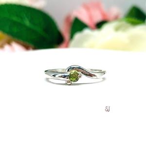 A silver round gemstone bypass ring with a thin band. The ring is set with a 3mm round peridot gemstone. The modern setting design curves around the gemstone. The ring is facing toward the back and is set against a white background.