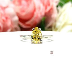 A sterling silver engagement ring set with a 9x6mm pear-cut canary yellow cz. Displayed on a white surface with soft pastel floral background.