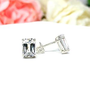 A pair of silver earrings with clear emerald cut lab created white sapphire stones. The earrings are on a white surface. The left earring is facing forward to showcase the crisp line faceting, and the right earring is facing the right to display the post at the top and butterfly friction clasp.