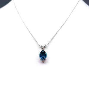 Close‑up of an oval‑cut teal blue lab gemstone sterling silver pendant suspended from a delicate silver chain. The pendant is the focal point, set against a white background.