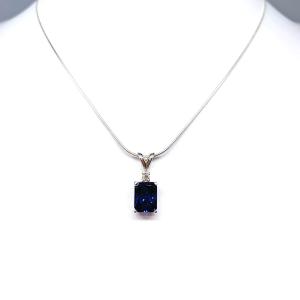 Sterling silver pendant featuring a 9x7mm radiant‑cut lab‑created blue sapphire with a 2.5mm round colorless moissanite accent above the sapphire. The pendant hangs from a fine silver chain against a clean white background, highlighting the vivid blue gemstone and polished metal finish.