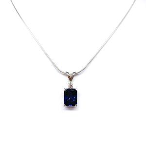 Sterling silver pendant featuring a 9x7mm radiant‑cut lab‑created blue sapphire with a 2.5mm round colorless moissanite accent above the sapphire. The pendant hangs from a fine silver chain against a clean white background, highlighting the vivid blue gemstone and polished metal finish.