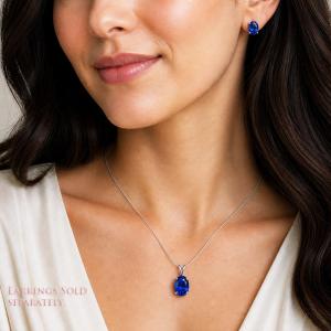 A woman wearing matching lab blue sapphire oval stud earrings and pendant necklace. 'EARRINGS SOLD SEPARATELY' appears in pink text in the image. Model image for size and styling reference — not a photo of the actual necklace.