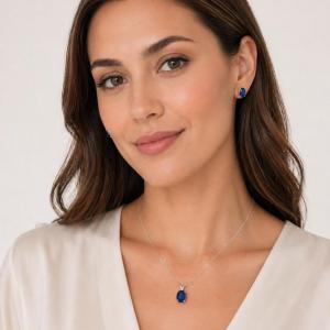 A woman wearing oval lab blue sapphire sterling silver stud earrings and matching pendant necklace. The text, 'IMAGE FOR STYLING REFERENCE ONLY - SEE LISTING FOR EXACT ITEM DETAILS. PENDANT NECKLACE SOLD SEPARATELY' appears in pink text at the bottom of the image. Model image for size and styling reference — not a photo of the actual jewelry.
