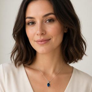 Headshot of a woman wearing oval‑cut teal blue lab gemstone pendant suspended on a chain in sterling silver. Model image for size and styling reference — not a photo of the actual necklace.