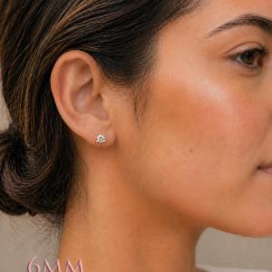 A woman wearing 6mm round 3-prong martini moissanite stud earrings. martini three prong moissanite stud earrings. Model image for size and styling reference — not a photo of the actual earrings.