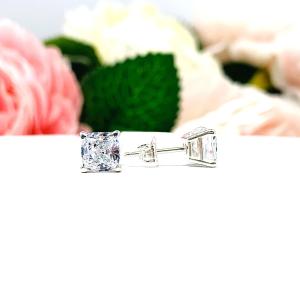 A pair of silver stud earrings with "crushed ice" cushion cut clear cubic zirconia stones. The basket style soft claw prong earrings are on a white surface. The left earring is facing forward to showcase the dazzling faceting of the crushed ice effect and the right earring is facing toward the right displaying the center placed post and butterfly friction clasp.