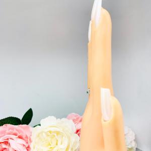 Mannequin hand with long white shimmery nails, displayed against a soft white-gray background with pink and white floral accents. The hand is wearing a sterling silver  five-stone curved wedding band with three 3mm round lab-created emeralds and two 3mm round DEF moissanites.