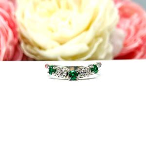 Sterling silver five-stone curved wedding band with three 3mm round lab-created emeralds and two 3mm round DEF moissanites, shown against a soft floral background.