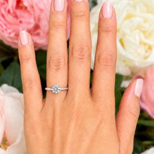 Woman's hand wearing a sterling silver 6.5mm round-cut 4-prong moissanite engagement ring. Model image for size and styling reference — not a photo of the actual ring.