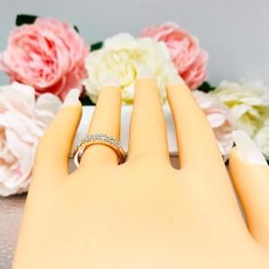 Mannequin hand with long white shimmery nails, displayed against a soft white-gray background with pink and white floral accents. The hand is wearing a sterling silver stackable 5-stone wedding band featuring 3mm round authentic moissanite stones in prong settings.