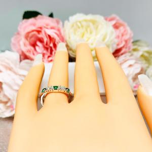 Mannequin hand with long white shimmery nails, displayed against a soft white-gray background with pink and white floral accents. The hand is wearing a sterling silver  five-stone curved wedding band with three 3mm round lab-created emeralds and two 3mm round DEF moissanites.