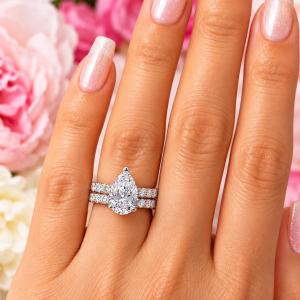 A woman's hand wearing an elegant sterling silver engagement ring set featuring a 12x8mm precision-cut pear cubic zirconia with pave CZ accents in a half eternity band. Shown with optional matching half-eternity band, designed to nest seamlessly. Model image for size and styling reference — not a photo of the actual ring.
