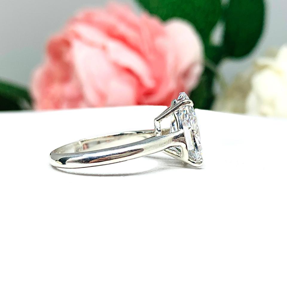 Elegant 4-prong sterling silver cathedral engagement ring set featuring a 12x8mm precision-cut pear cubic zirconia.  Displayed on a white surface with soft pastel floral background.