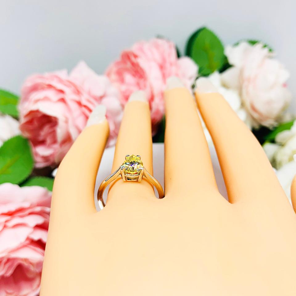 Mannequin hand with long white shimmery nails, displayed against a soft white-gray background with pink and white floral accents. The hand is wearing a sterling silver engagement ring set with a 9x6mm pear-cut canary yellow cz.