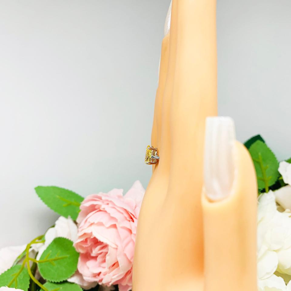 Mannequin hand with long white shimmery nails, displayed against a soft white-gray background with pink and white floral accents. The hand is wearing a sterling silver engagement ring set with a 9x6mm pear-cut canary yellow cz.