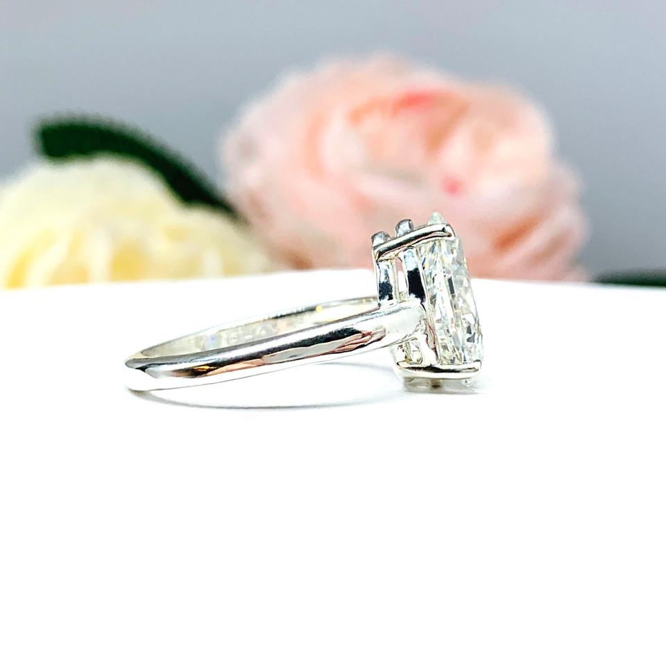 An elegant 4-prong sterling silver engagement ring with a 3mm wide band featuring a 13x9mm near colorless precision-cut pear cubic zirconia. Displayed on a white surface with a floral background.