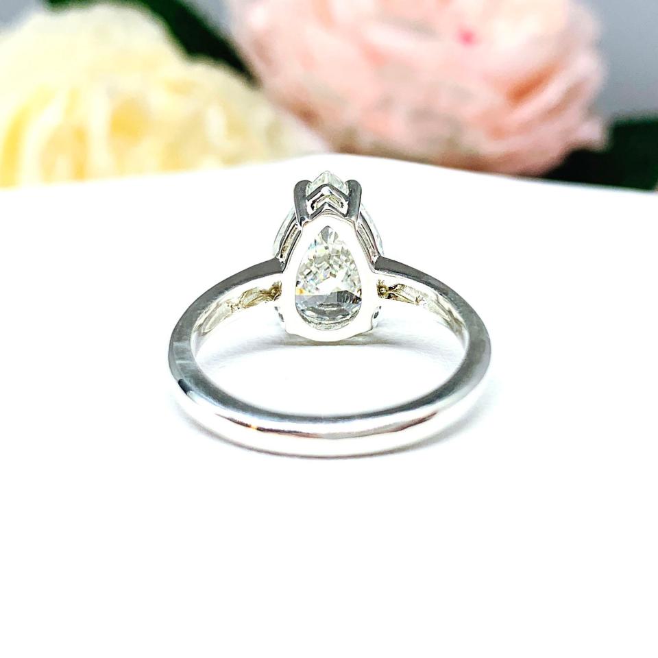 An elegant 4-prong sterling silver engagement ring with a 3mm wide band featuring a 13x9mm near colorless precision-cut pear cubic zirconia. Displayed on a white surface with a floral background.