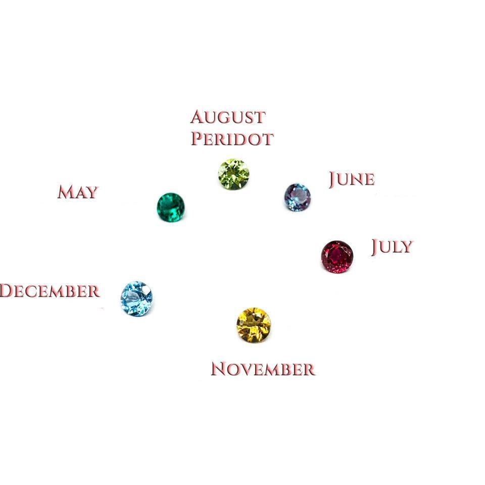 A composite photo of six gemstones on a white background. Each gemstone is labeled with pink text. The gemstones appear in a circular fashion, in this order with these colors and corresponding text, clockwise: light olive green 'August', purplish green 'June', deep red 'July', golden yellow 'November', bright blue 'December', and emerald green 'May'.
