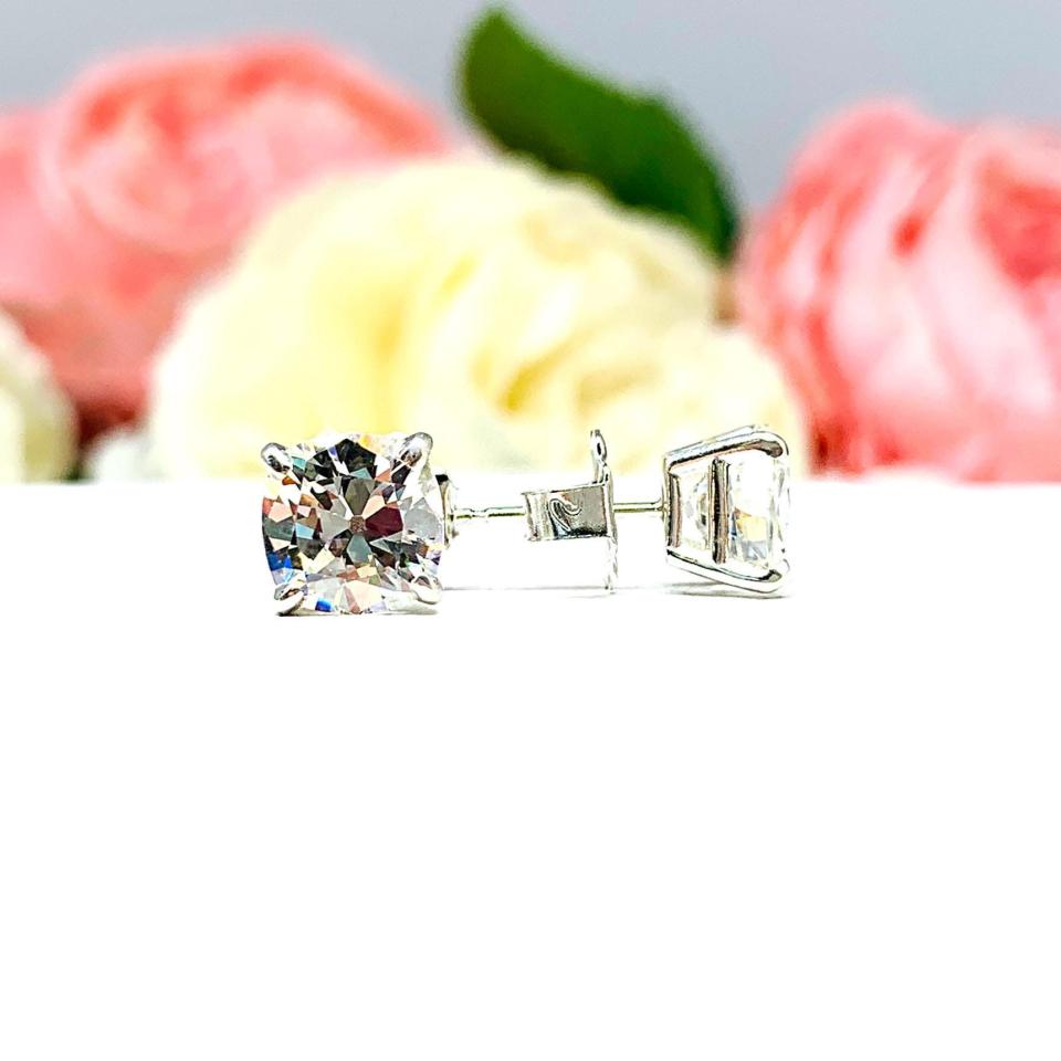 A pair of silver stud earrings with very light yellow or "near colorless" old mine cut cubic zirconia stones. The basket style soft claw prong earrings are on a white background with the left earring facing forward to showcase the 'chunky' facets and the right earring facing to the right displaying the center post and butterfly friction clasps.