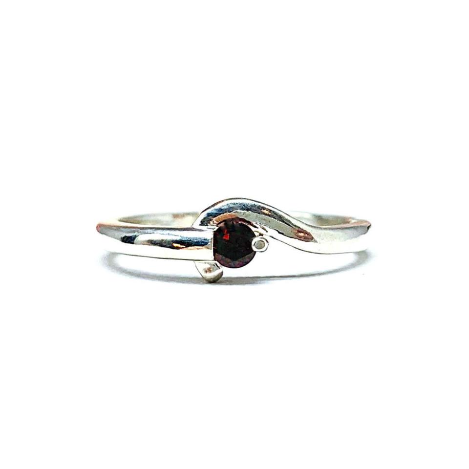 A sterling silver round gemstone bypass ring with a thin band. The ring is set with a 3mm round Mozambique garnet gemstone. The modern setting design curves around the gemstone. The ring is facing toward the back and is set against a white background.