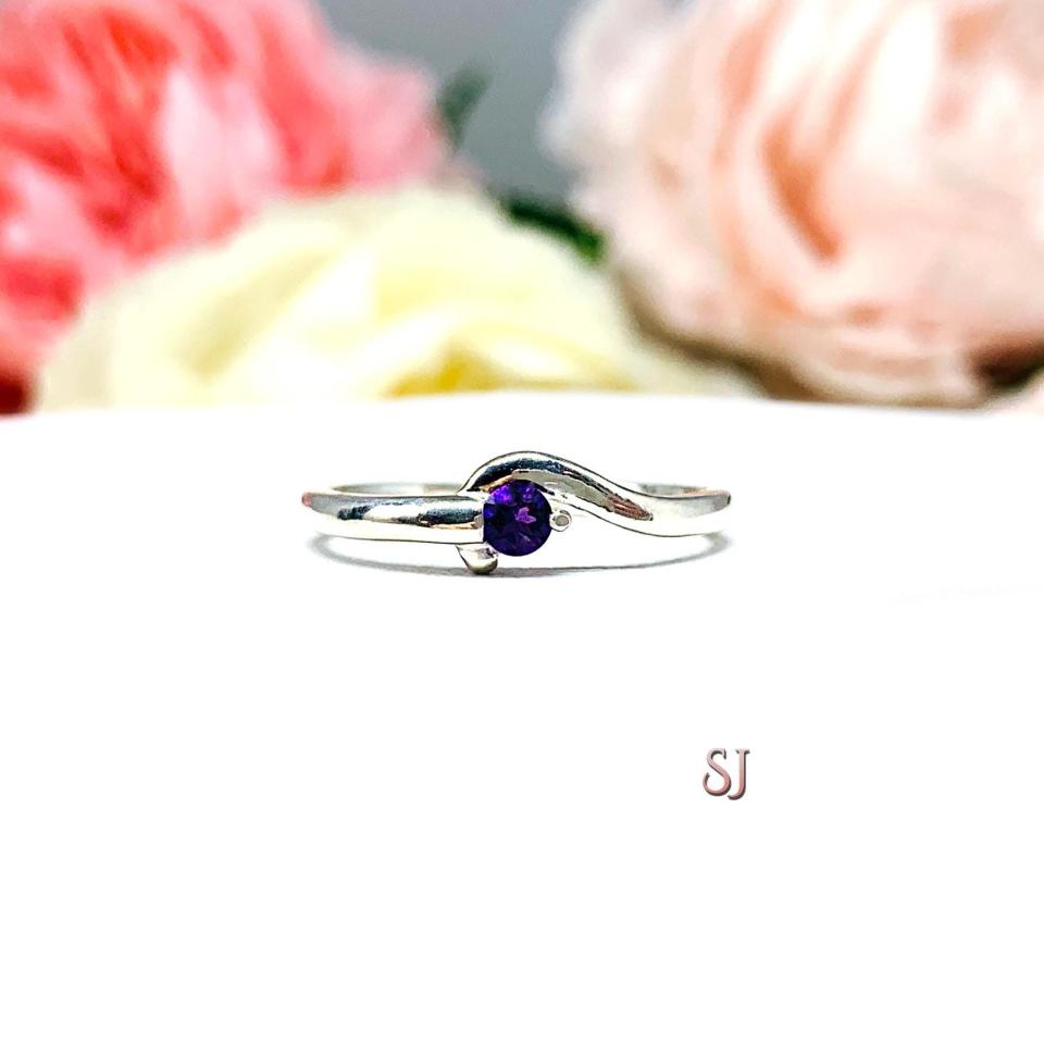 A sterling silver round gemstone bypass ring with a thin band. The ring is set with 3mm round African amethyst gemstone. The modern setting design curves around the gemstone. The ring is facing toward the back and is set against a white background.