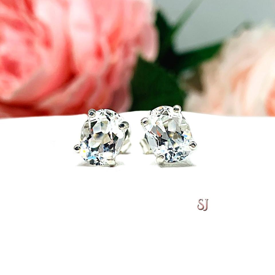 A pair of silver basket earrings set with oval natural white topaz gemstones. Both earrings are facing forward to showcase the clear clarity of the stones.
