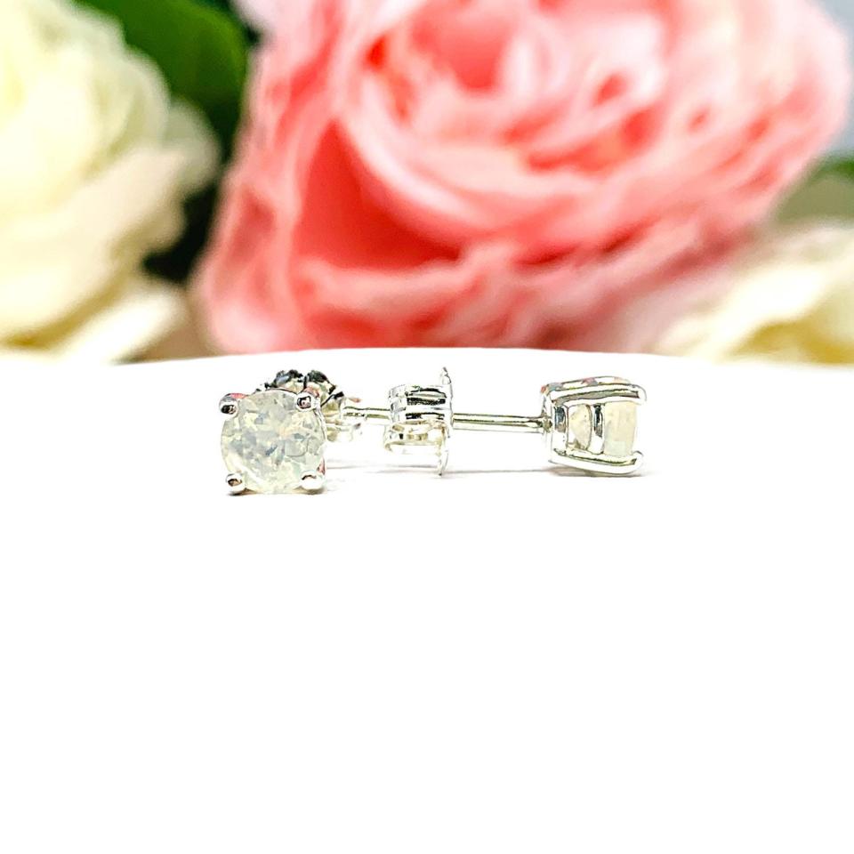 A pair of silver basket stud earrings set with round Contra Luz precious opal gemstones. The four prong earrings are set against a white background with the left earring facing forward showcasing the irridescence of the gemstones and the right earring facing toward the right to display the center post and butterfly friction clasp.