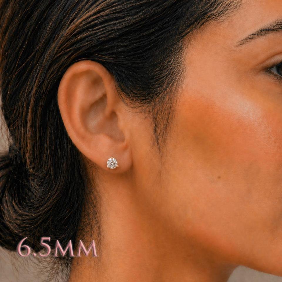 A woman wearing 6.5mm round 3-prong martini moissanite stud earrings. martini three prong moissanite stud earrings. Model image for size and styling reference — not a photo of the actual earrings.