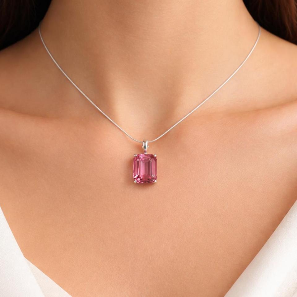 A sterling silver necklace with a 12x10mm emerald-cut deep tone padparadscha pink pendant. The pendant is suspended from a delicate silver snake chain. The woman is wearing a white top. Model image for size and styling reference — not a photo of the actual necklace.