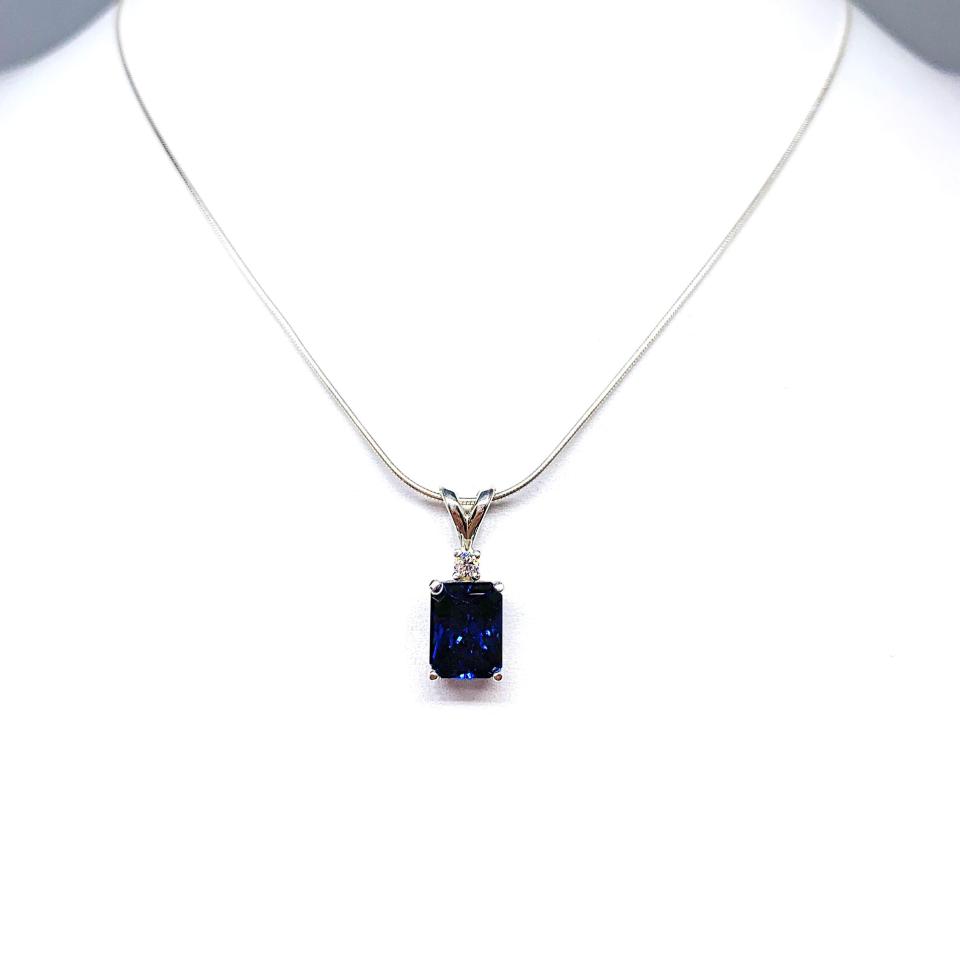 Sterling silver pendant featuring a 9x7mm radiant‑cut lab‑created blue sapphire with a 2.5mm round colorless moissanite accent above the sapphire. The pendant hangs from a fine silver chain against a clean white background, highlighting the vivid blue gemstone and polished metal finish.