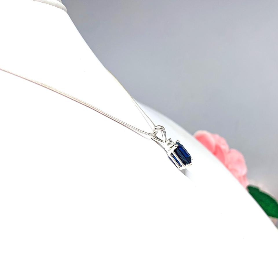 Sterling silver pendant featuring a 9x7mm radiant‑cut lab‑created blue sapphire with a 2.5mm round colorless moissanite accent above the sapphire. The pendant hangs from a fine silver chain against a clean white background, highlighting the vivid blue gemstone and polished metal finish.