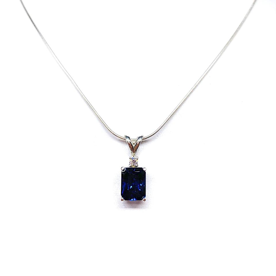 Sterling silver pendant featuring a 9x7mm radiant‑cut lab‑created blue sapphire with a 2.5mm round colorless moissanite accent above the sapphire. The pendant hangs from a fine silver chain against a clean white background, highlighting the vivid blue gemstone and polished metal finish.