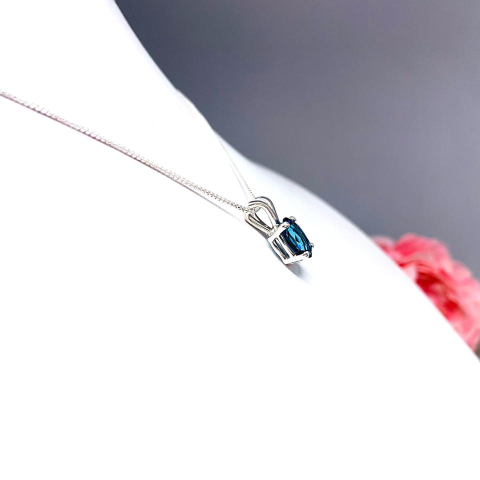 Close‑up of an oval‑cut teal blue lab gemstone sterling silver pendant suspended from a delicate silver chain. The pendant is the focal point, set against a white background.