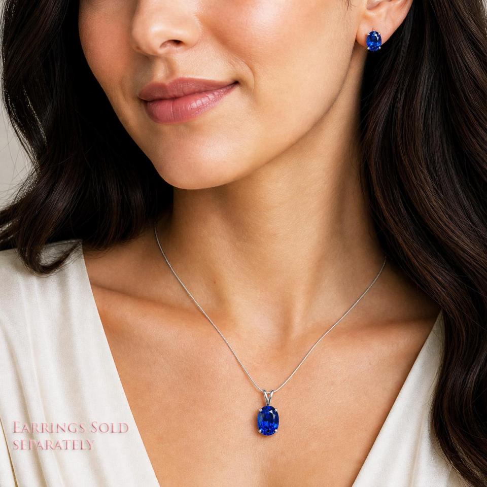 A woman wearing matching lab blue sapphire oval stud earrings and pendant necklace. 'EARRINGS SOLD SEPARATELY' appears in pink text in the image. Model image for size and styling reference — not a photo of the actual necklace.
