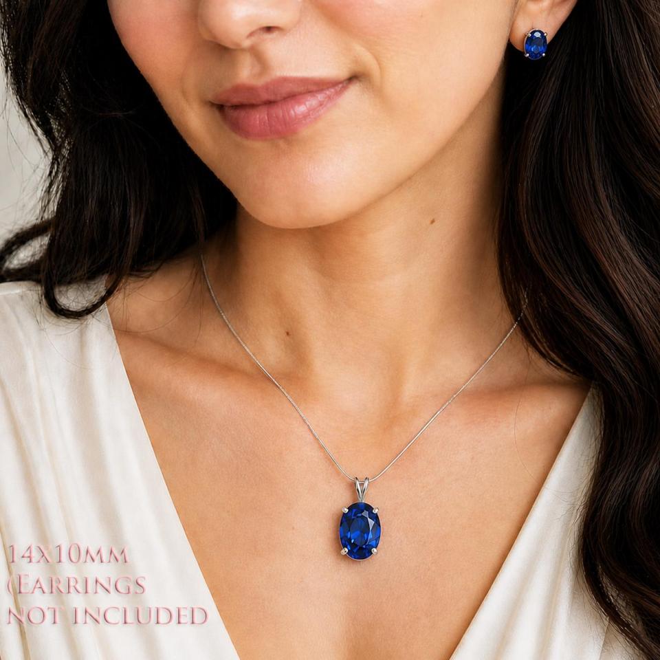 A woman wearing a 14x10mm lab blue sapphire oval sterling silver pendant necklace and smaller matching earrings. 'EARRINGS NOT INCLUDED' appears in pink text in the image. Model image for size and styling reference — not a photo of the actual necklace.