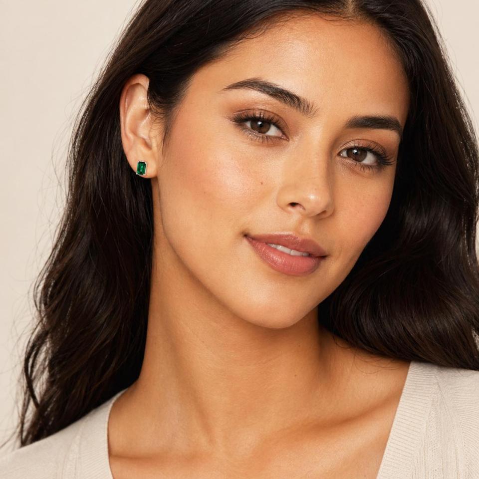 A woman wearing 7x5mm emerald cut lab emerald sterling silver stud earrings. Model image for size and styling reference — not a photo of the actual earrings.