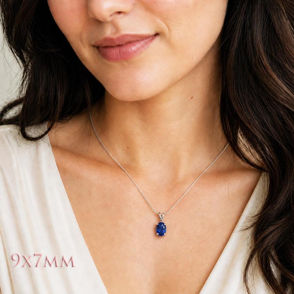 A woman wearing a 9x7mm lab blue sapphire oval sterling silver pendant necklace. Model image for size and styling reference — not a photo of the actual necklace.