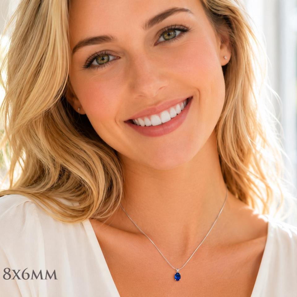 A woman wearing an 8x6mm lab blue sapphire oval sterling silver pendant necklace. Model image for size and styling reference — not a photo of the actual necklace.