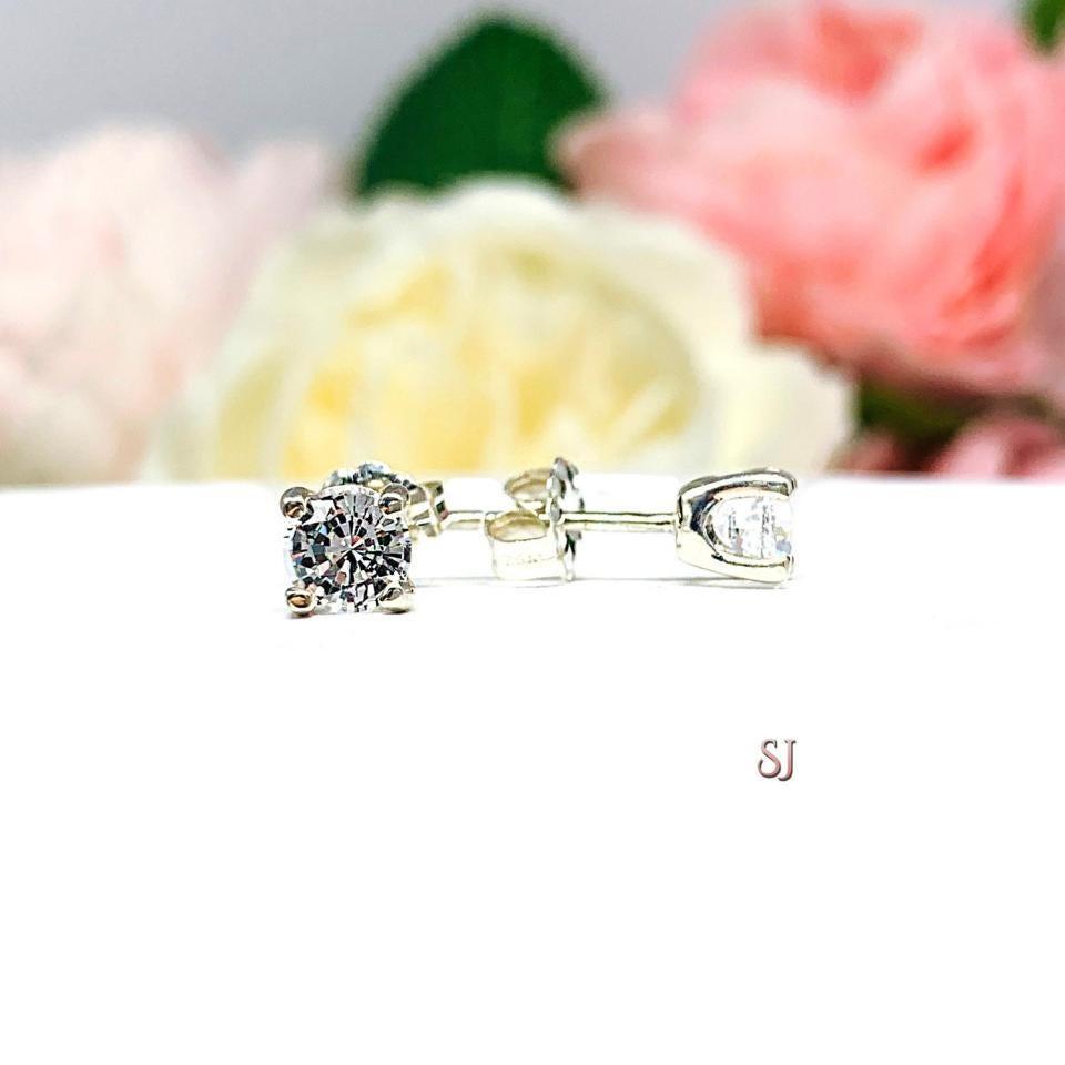 A pair of sterling silver 4-prong stud earrings set with round mixed brilliant lab white sapphires, displayed with one earring facing the front to showcase the faceting and one facing to the side to display center post and the butterfly friction clasp. The earrings are shown on a white background.