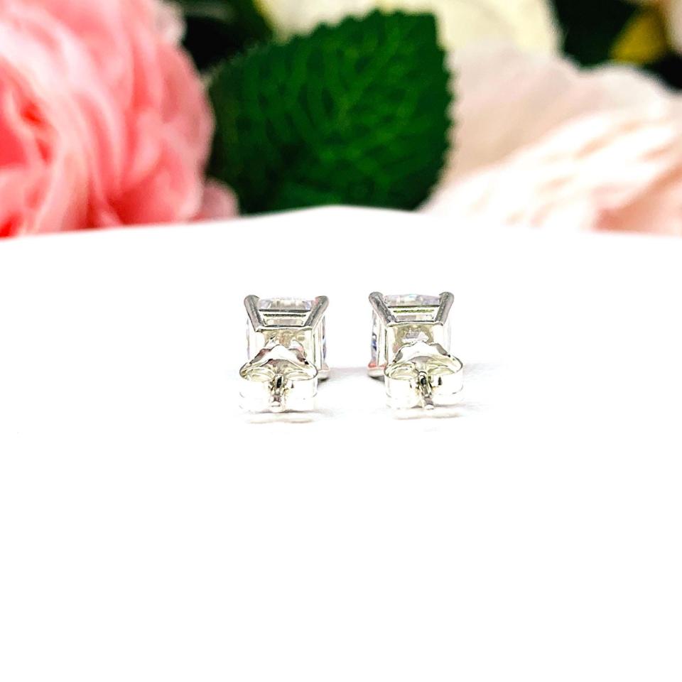 A pair of silver stud earrings with "crushed ice" cushion cut clear cubic zirconia stones. The basket style soft claw prong earrings are on a white surface. Both earrings are facing slightly toward the back displaying the center posts and butterfly clasps.