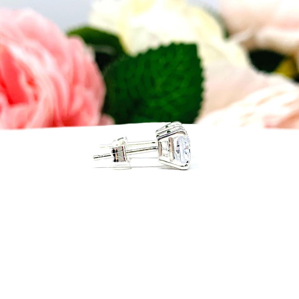 A pair of silver stud earrings with "crushed ice" cushion cut clear cubic zirconia stones. The basket style soft claw prong earrings are on a white surface. Both earrings are facing toward the right.